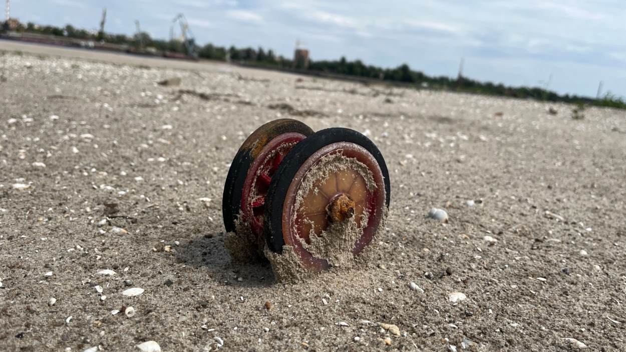 Колесо от детской коляски в песке. Много лет оно провело под водой, а теперь выглядит как в фильме ужасов.