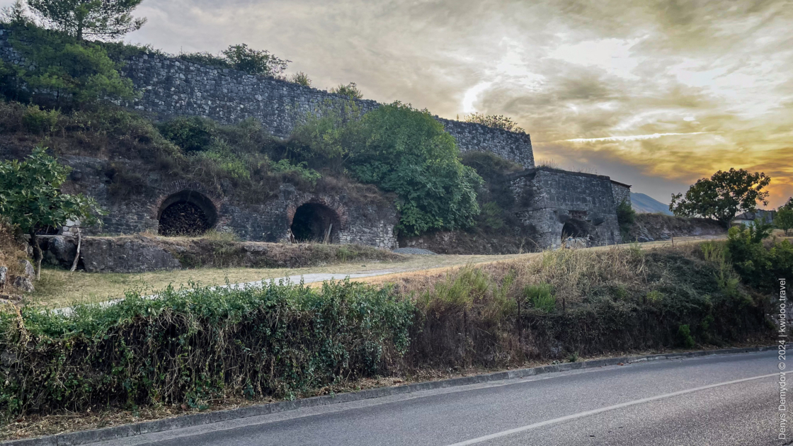 The walls of a medieval-style hotel in Albania, against a sunset-colored cloudy sky.